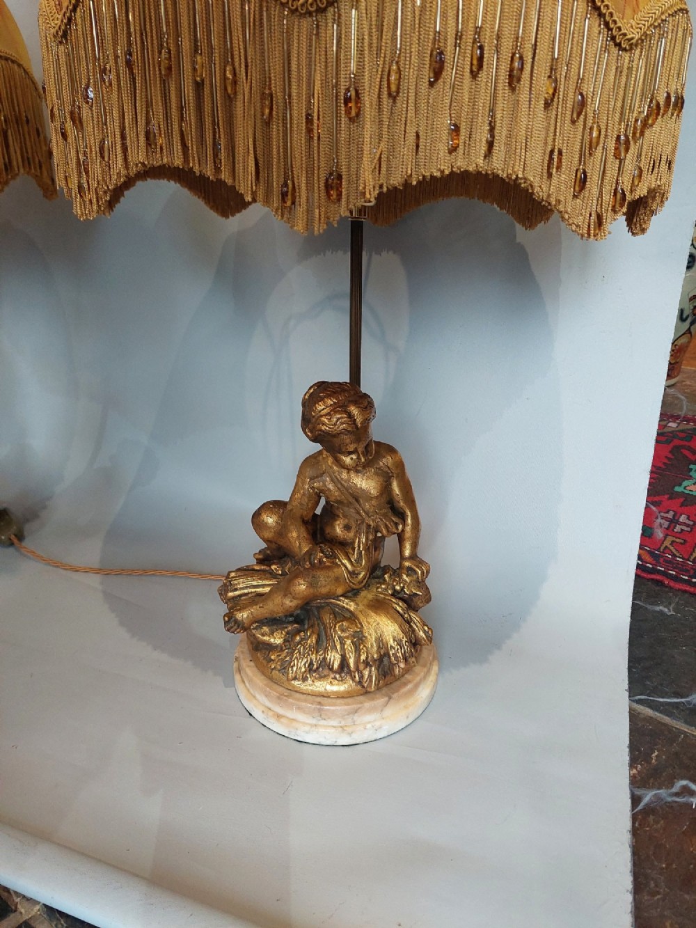 A pair of ornate table lamps featuring gilded cherub figures mounted on white alabaster bases, topped with fringed dome fabric shades. View III
