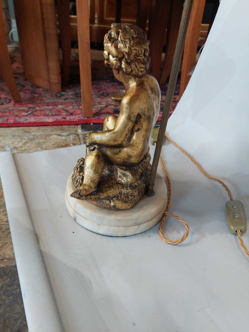 A pair of ornate table lamps featuring gilded cherub figures mounted on white alabaster bases, topped with fringed dome fabric shades. View V