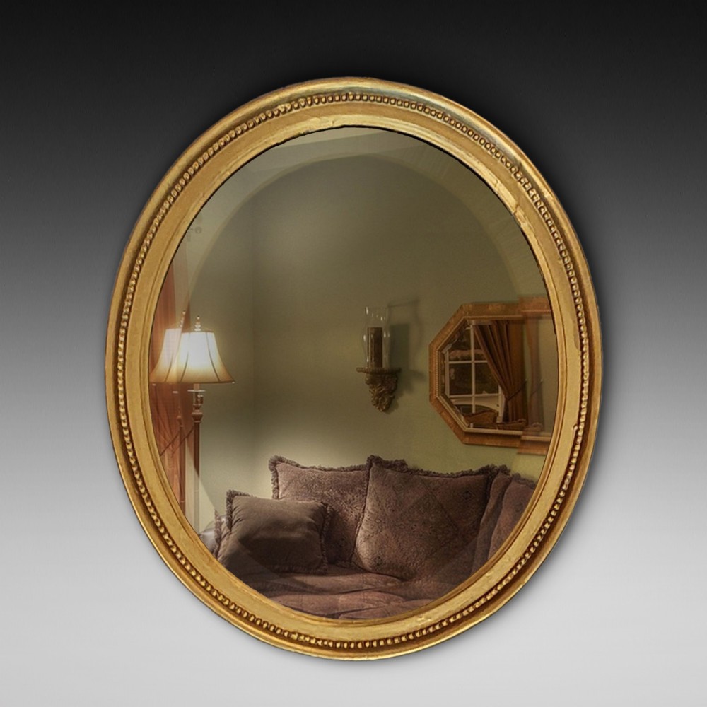 An oval 19th-century wall mirror featuring a giltwood frame with a beaded inner border.