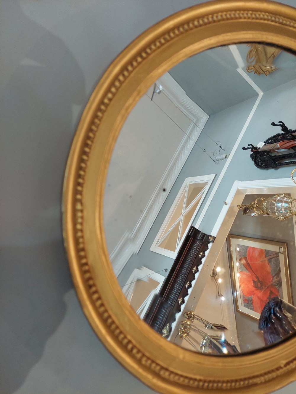 An oval 19th-century wall mirror featuring a giltwood frame with a beaded inner border. View II