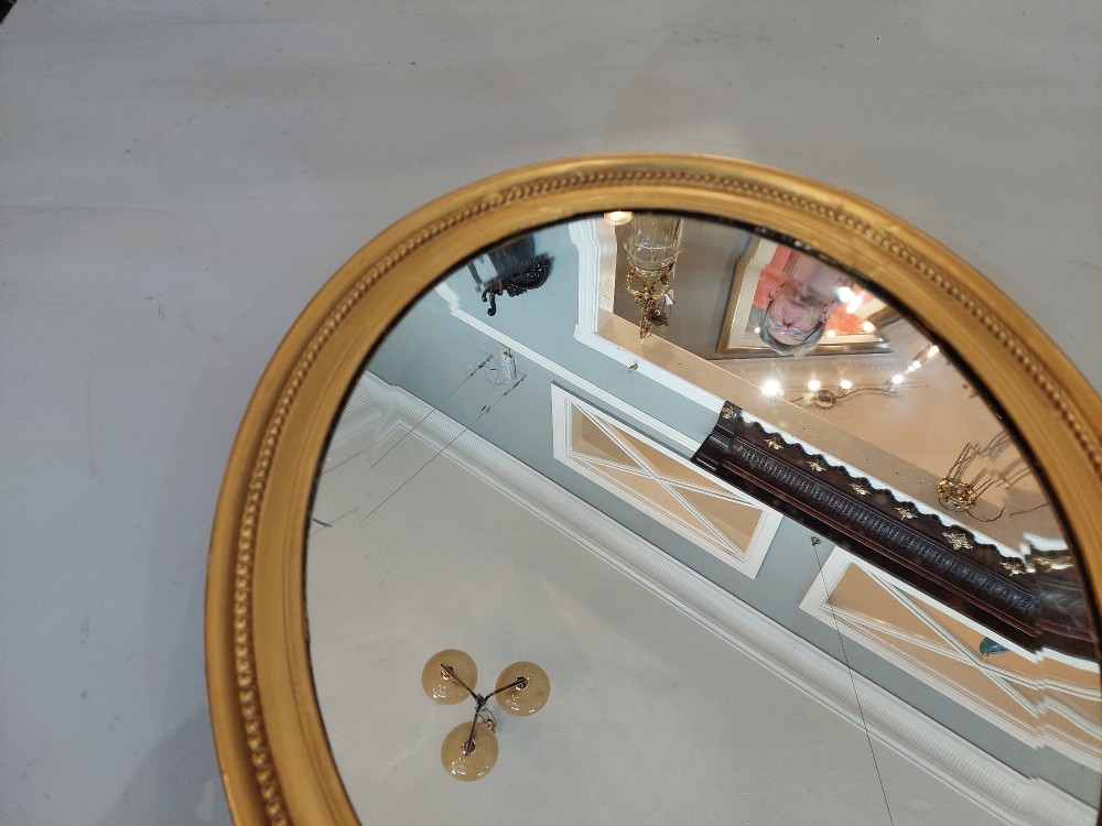 An oval 19th-century wall mirror featuring a giltwood frame with a beaded inner border. View III