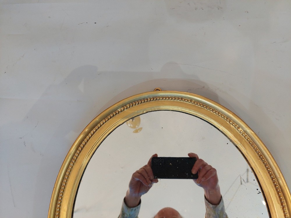 An oval 19th-century wall mirror featuring a giltwood frame with a beaded inner border. View IV