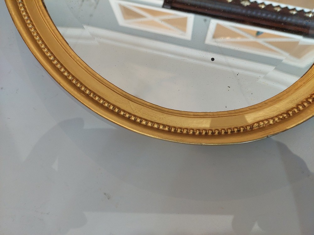 An oval 19th-century wall mirror featuring a giltwood frame with a beaded inner border. View V