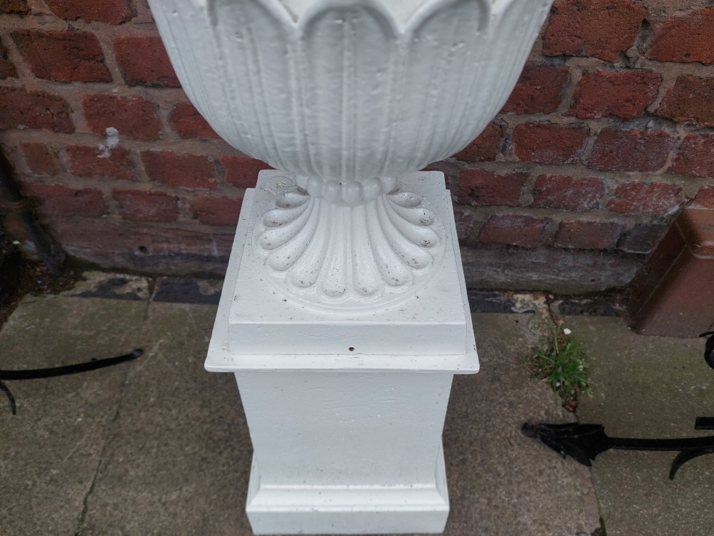 A classical white painted garden urn featuring an acanthus leaf pattern and scalloped rim, positioned on a matching square pedestal stand. View III