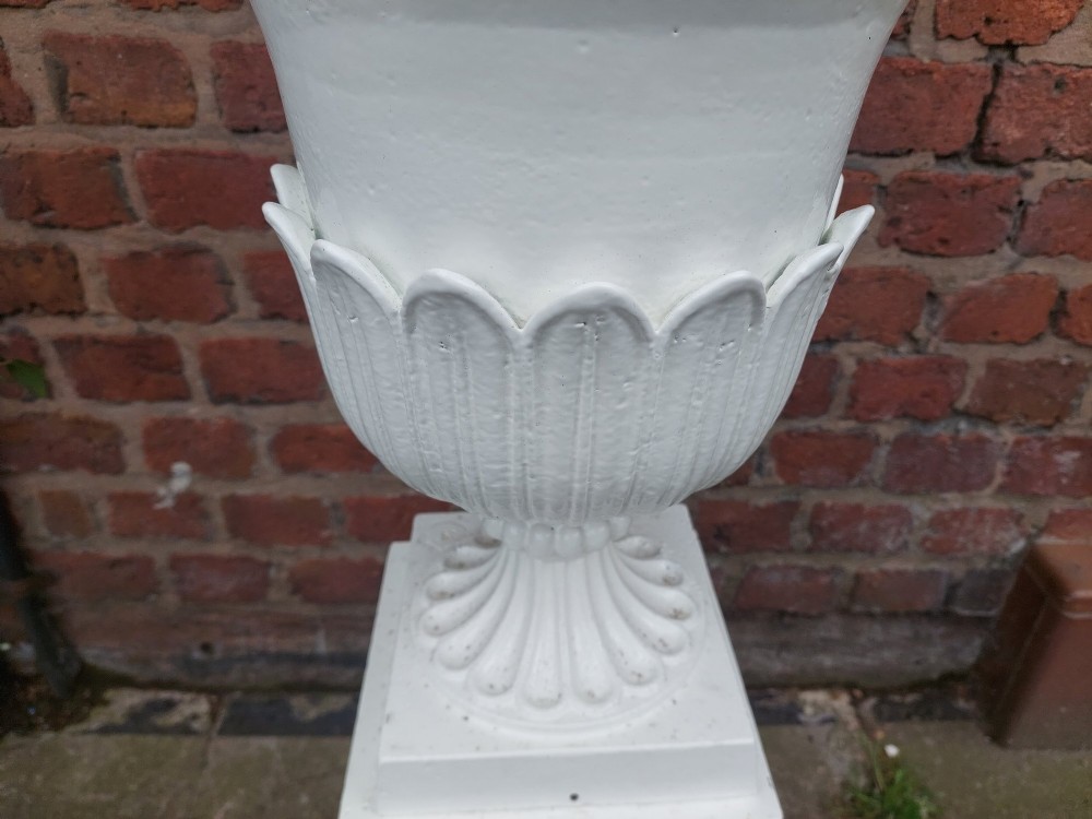 A classical white painted garden urn featuring an acanthus leaf pattern and scalloped rim, positioned on a matching square pedestal stand. View IV