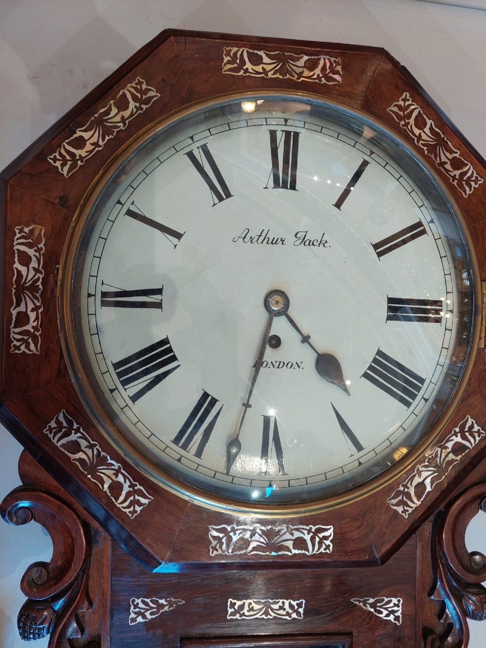 A Victorian octagonal rosewood wall clock featuring intricate floral mother-of-pearl inlay, carved side scrolls, and an off-white dial with Roman numerals. View II