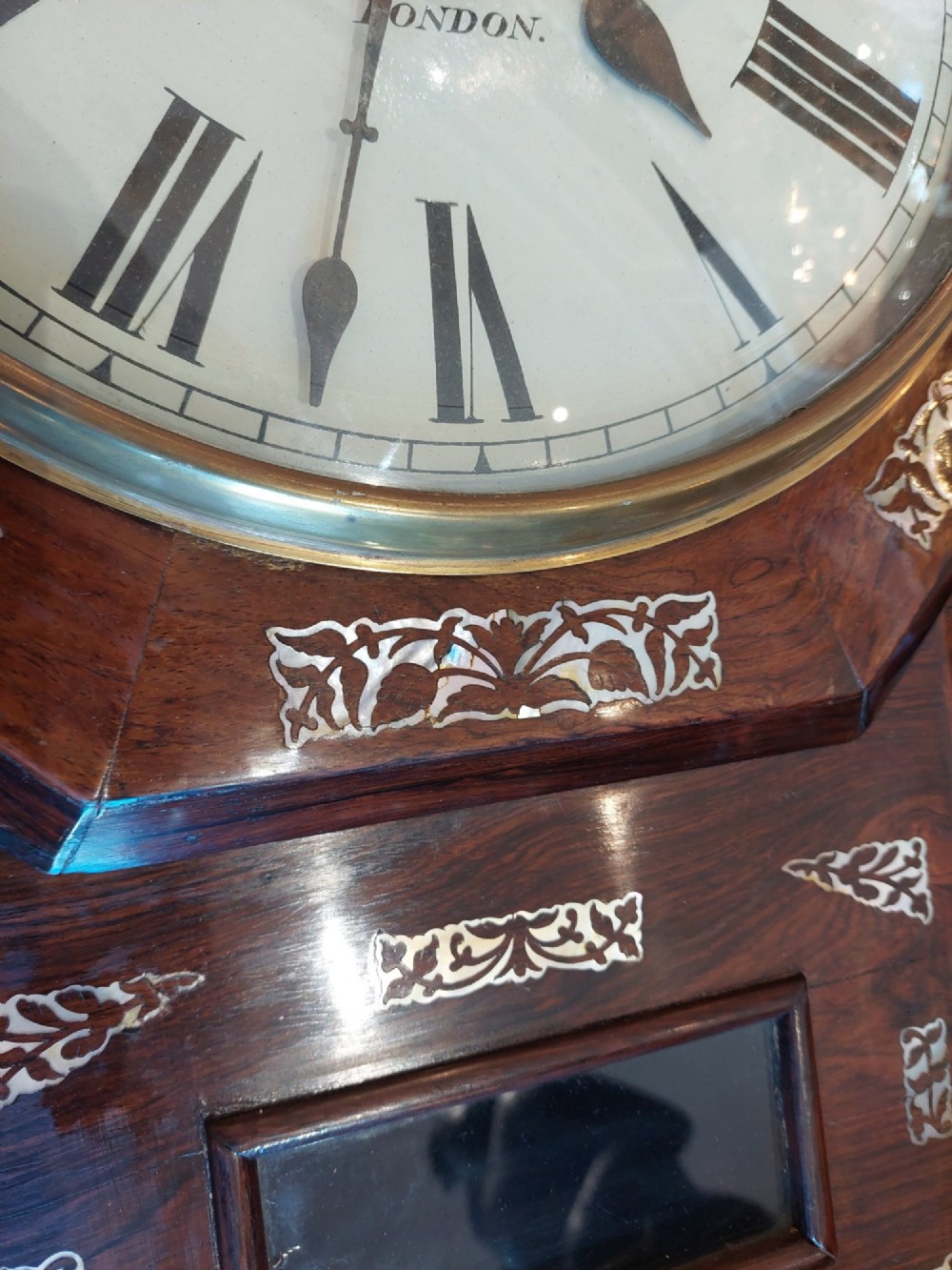 A Victorian octagonal rosewood wall clock featuring intricate floral mother-of-pearl inlay, carved side scrolls, and an off-white dial with Roman numerals. View V
