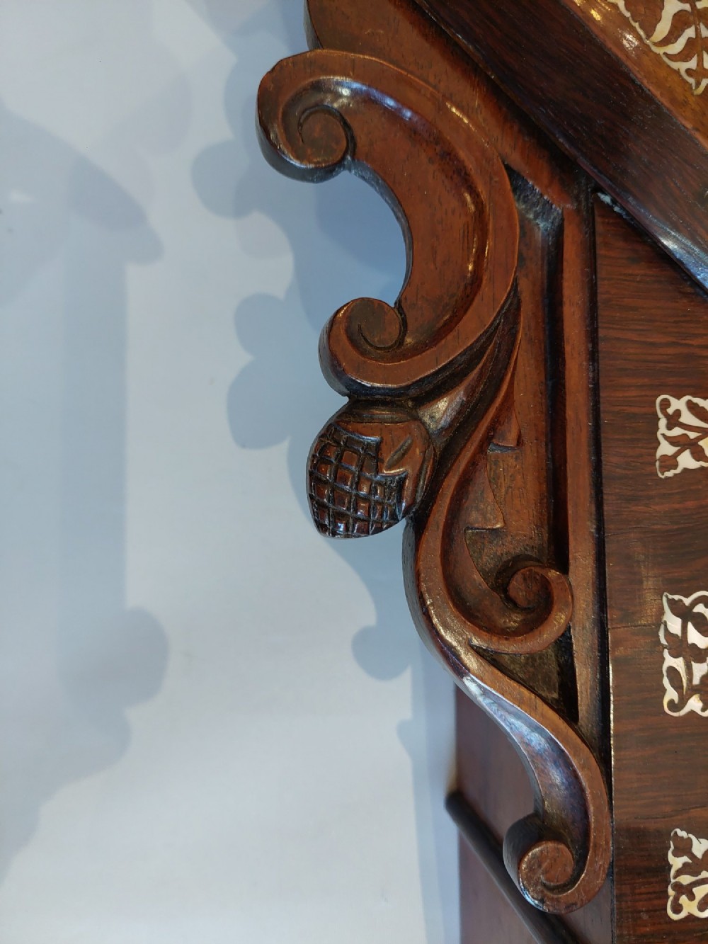 A Victorian octagonal rosewood wall clock featuring intricate floral mother-of-pearl inlay, carved side scrolls, and an off-white dial with Roman numerals. View VI