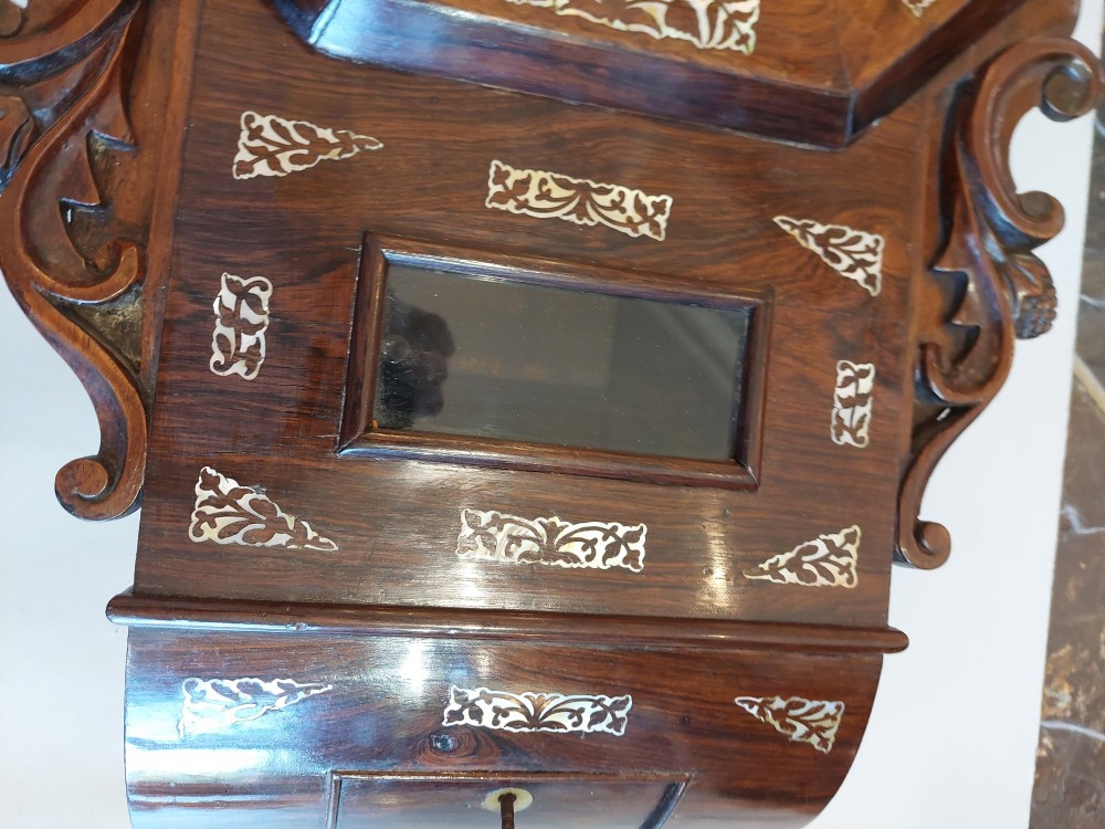 A Victorian octagonal rosewood wall clock featuring intricate floral mother-of-pearl inlay, carved side scrolls, and an off-white dial with Roman numerals. View VIII