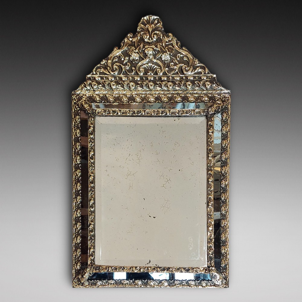 An antique 19th-century French rectangular wall mirror featuring an embossed pressed brass frame with a decorated triangular crest and mirrored border surround.
