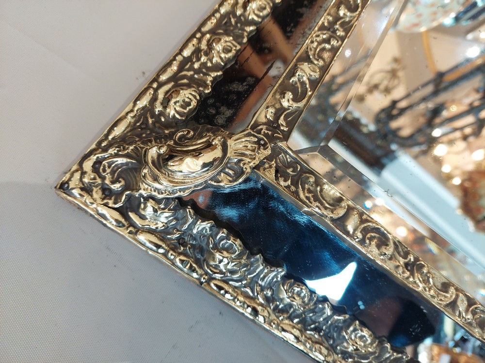 An antique 19th-century French rectangular wall mirror featuring an embossed pressed brass frame with a decorated triangular crest and mirrored border surround. View VI