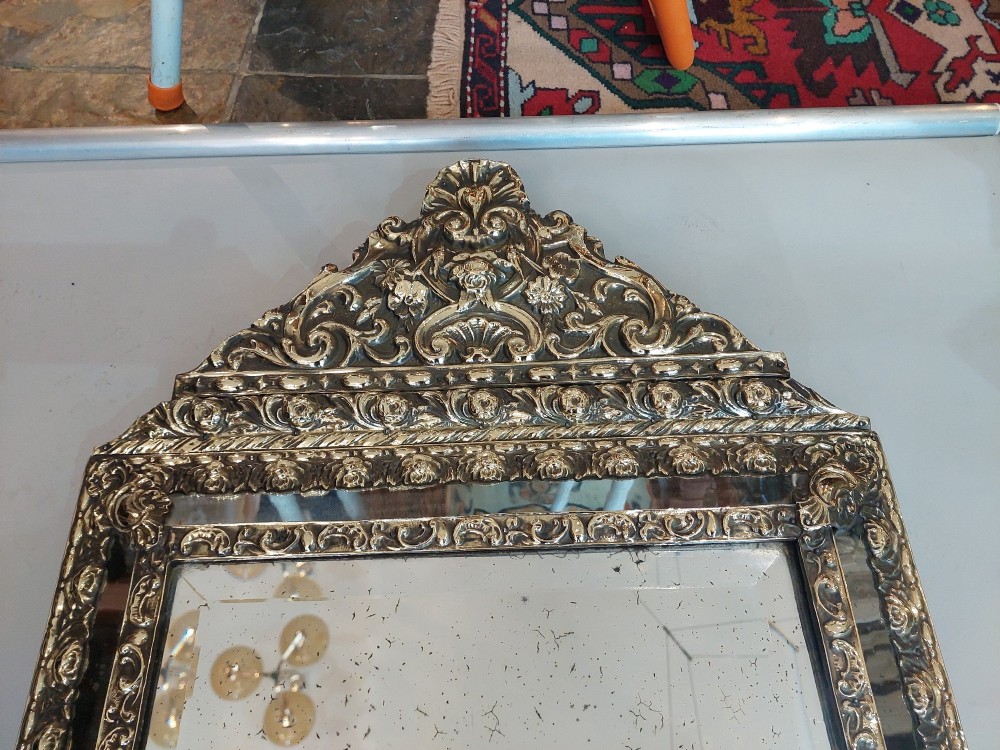 An antique 19th-century French rectangular wall mirror featuring an embossed pressed brass frame with a decorated triangular crest and mirrored border surround. View VII