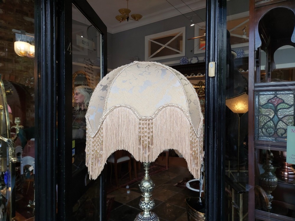A pair of ornate silvered brass standard lamps featuring detailed turned baluster stems, lobed bases, and cream domed fabric shades with fringed edging. View III