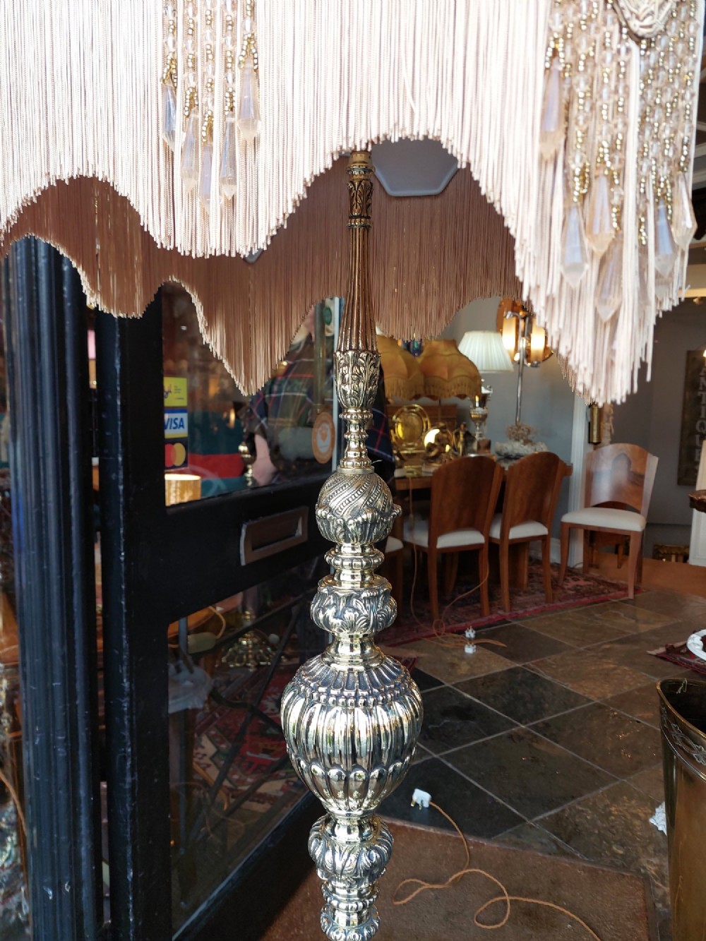 A pair of ornate silvered brass standard lamps featuring detailed turned baluster stems, lobed bases, and cream domed fabric shades with fringed edging. View V