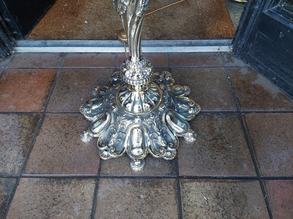A pair of ornate silvered brass standard lamps featuring detailed turned baluster stems, lobed bases, and cream domed fabric shades with fringed edging. View VIII