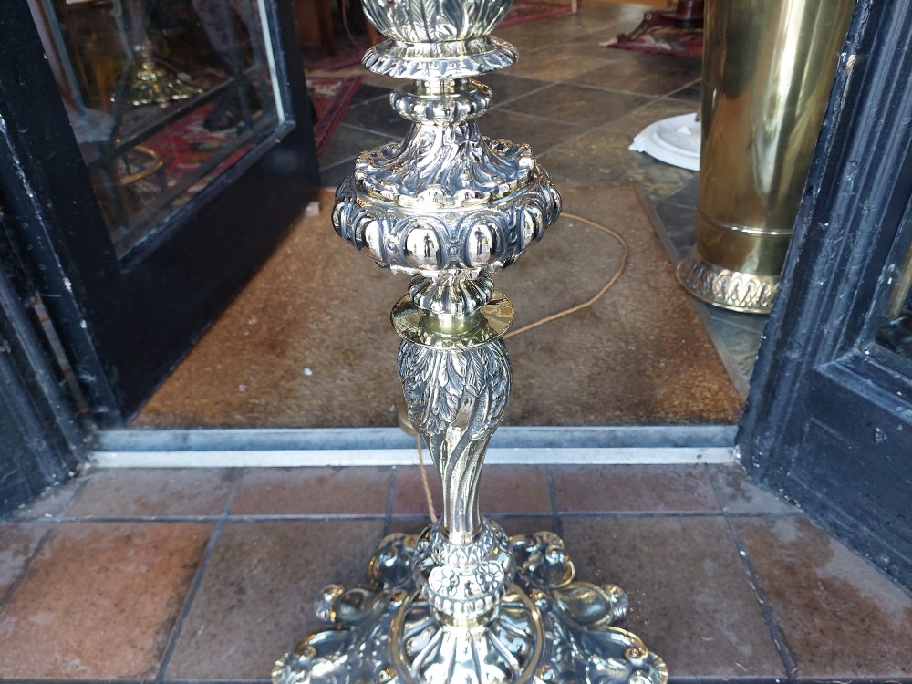 A pair of ornate silvered brass standard lamps featuring detailed turned baluster stems, lobed bases, and cream domed fabric shades with fringed edging. View IX