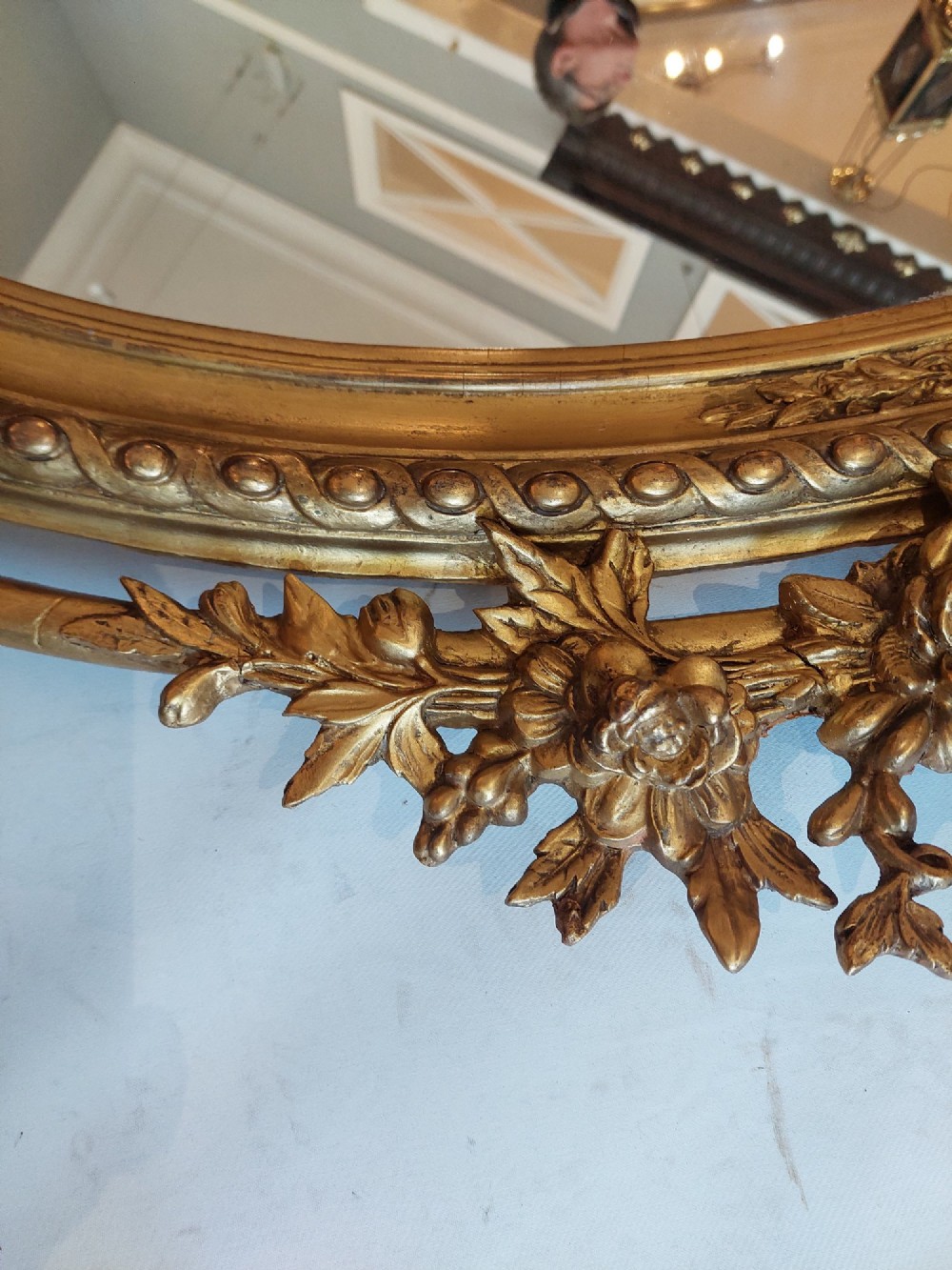 An oval 19th-century carved giltwood wall mirror featuring an intricate top crest with a torch and floral motif and an egg-and-dart inner frame border. View III