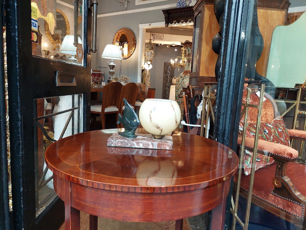 An Art Deco table lamp featuring a dark green patinated fish sculpture alongside a spherical cream glass shade, set on a rectangular variegated marble base. View II