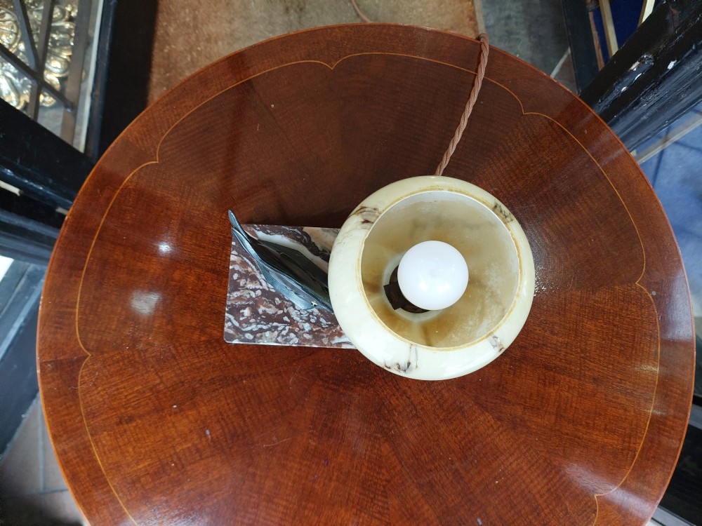 An Art Deco table lamp featuring a dark green patinated fish sculpture alongside a spherical cream glass shade, set on a rectangular variegated marble base. View V
