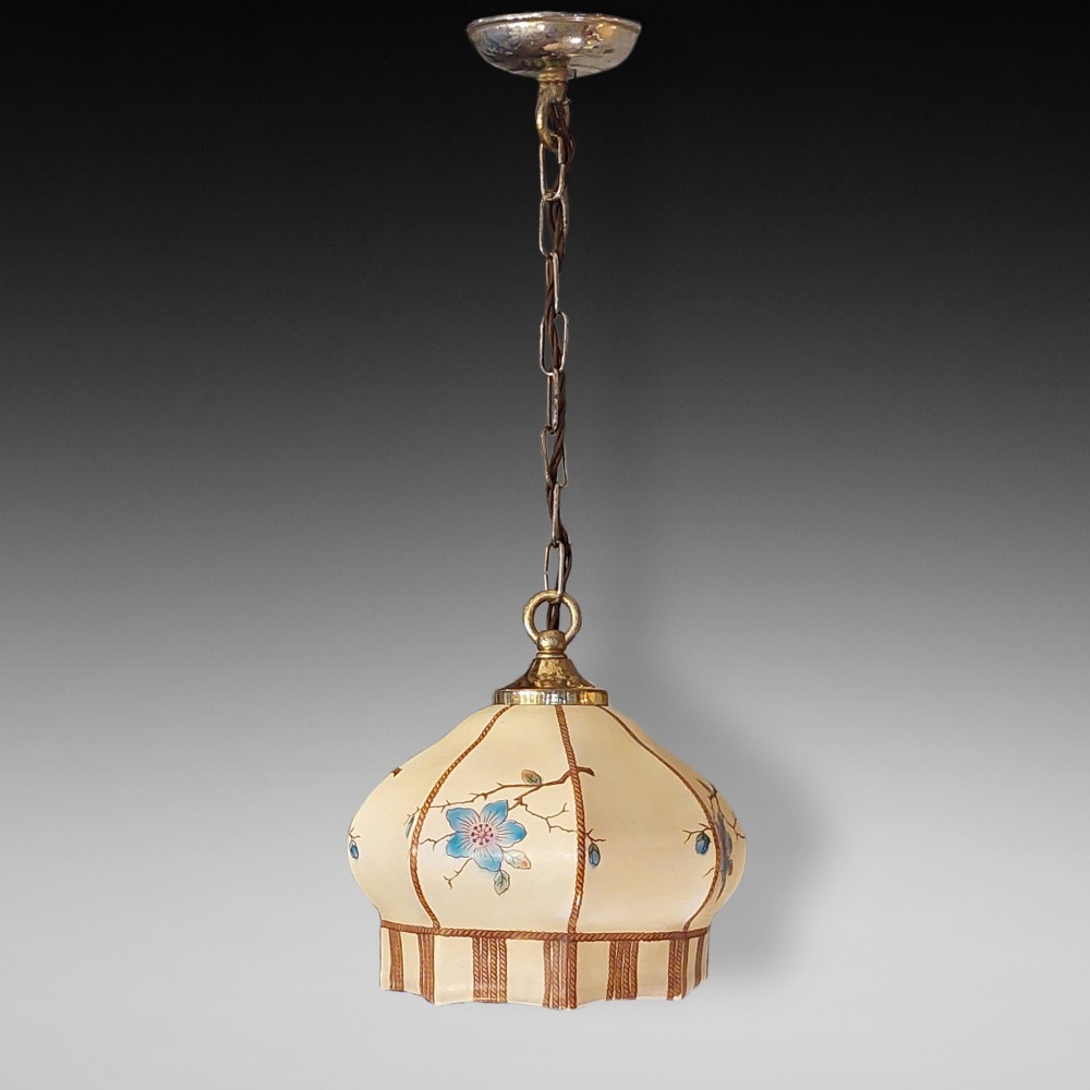 A 1920s cream glass pendant light shade hand painted with blue floral motifs, suspended from a brass chain.