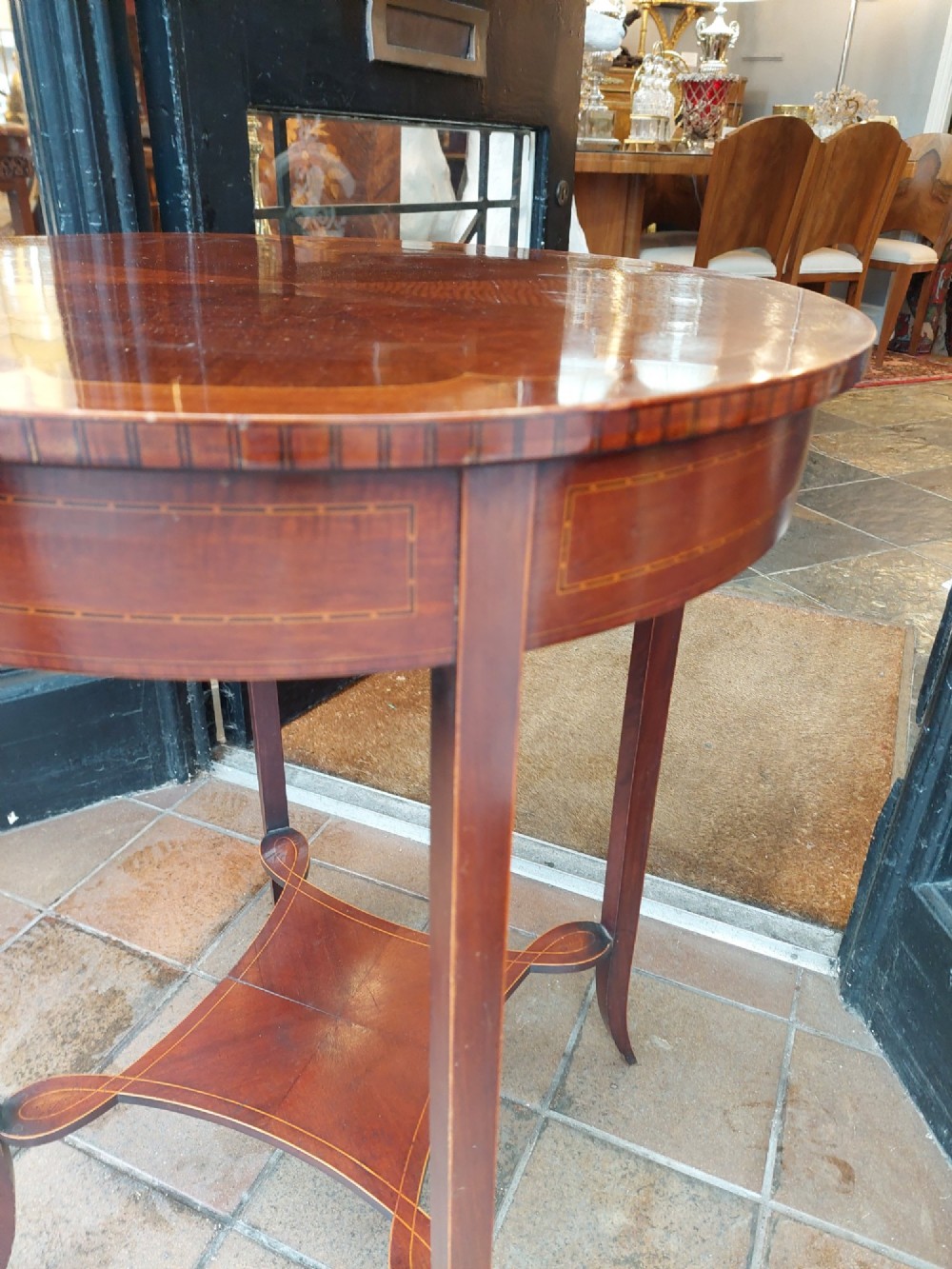 A circular Edwardian mahogany occasional table featuring a segmented veneer top with boxwood stringing inlay, splayed legs, and a lower concave stretcher shelf. View IV