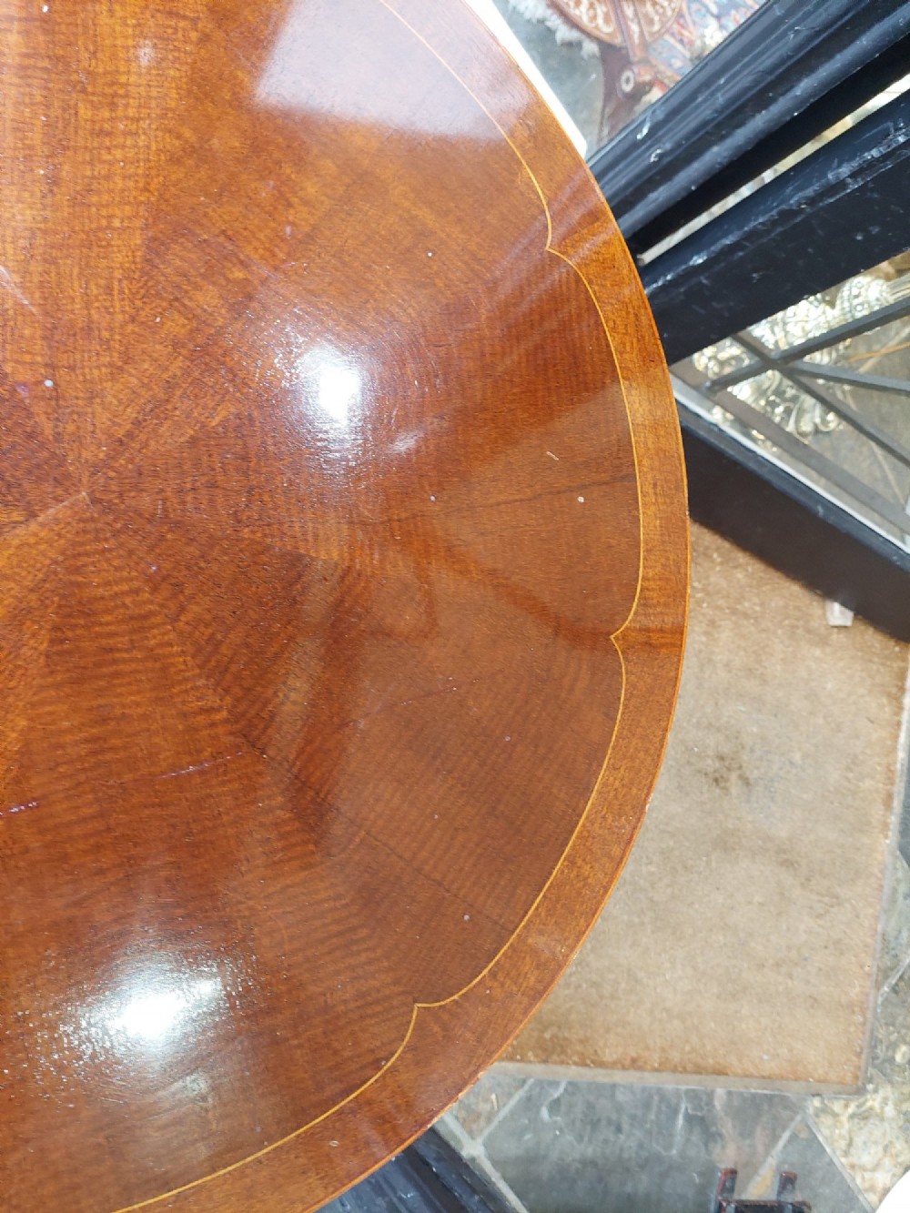 A circular Edwardian mahogany occasional table featuring a segmented veneer top with boxwood stringing inlay, splayed legs, and a lower concave stretcher shelf. View V