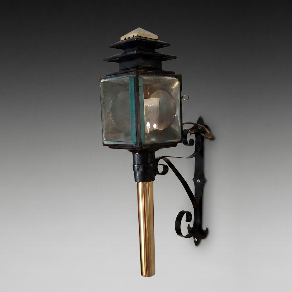 An antique black iron and polished brass carriage lamp mounted on a decorative scrolled wall bracket with bevelled glass panels.