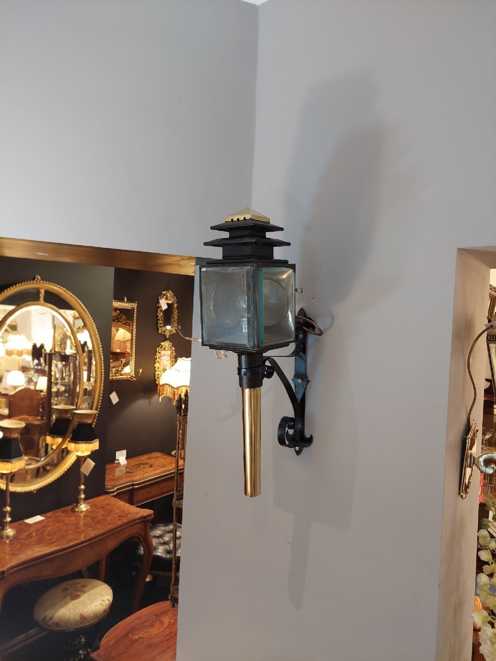 An antique black iron and polished brass carriage lamp mounted on a decorative scrolled wall bracket with bevelled glass panels. View II
