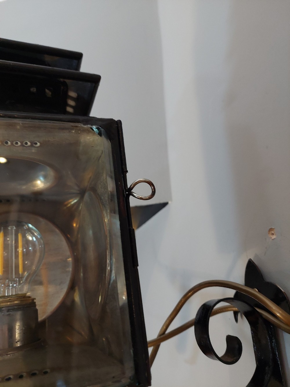 An antique black iron and polished brass carriage lamp mounted on a decorative scrolled wall bracket with bevelled glass panels. View III
