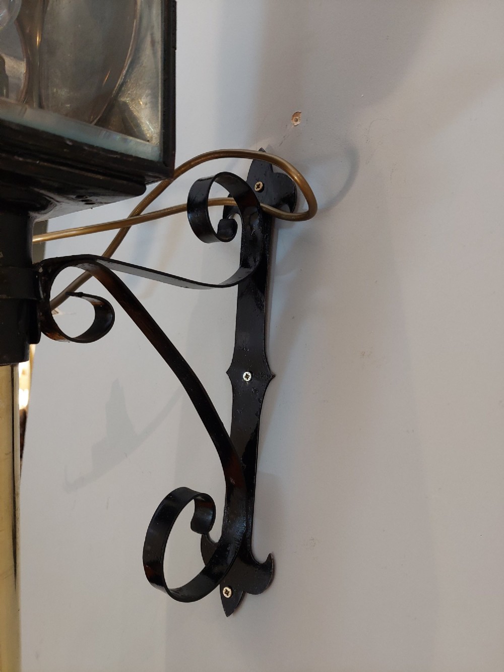 An antique black iron and polished brass carriage lamp mounted on a decorative scrolled wall bracket with bevelled glass panels. View VI