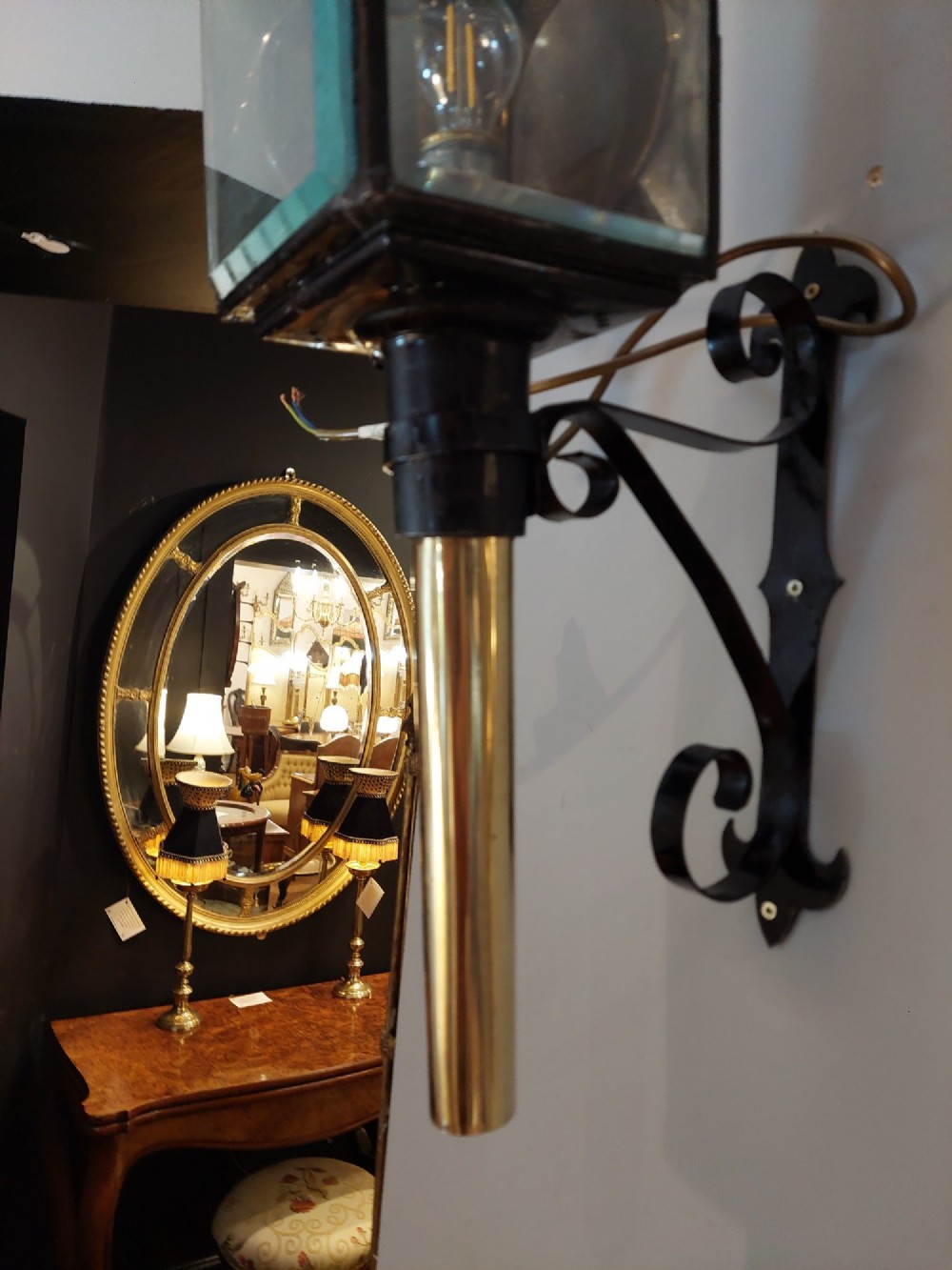 An antique black iron and polished brass carriage lamp mounted on a decorative scrolled wall bracket with bevelled glass panels. View VII