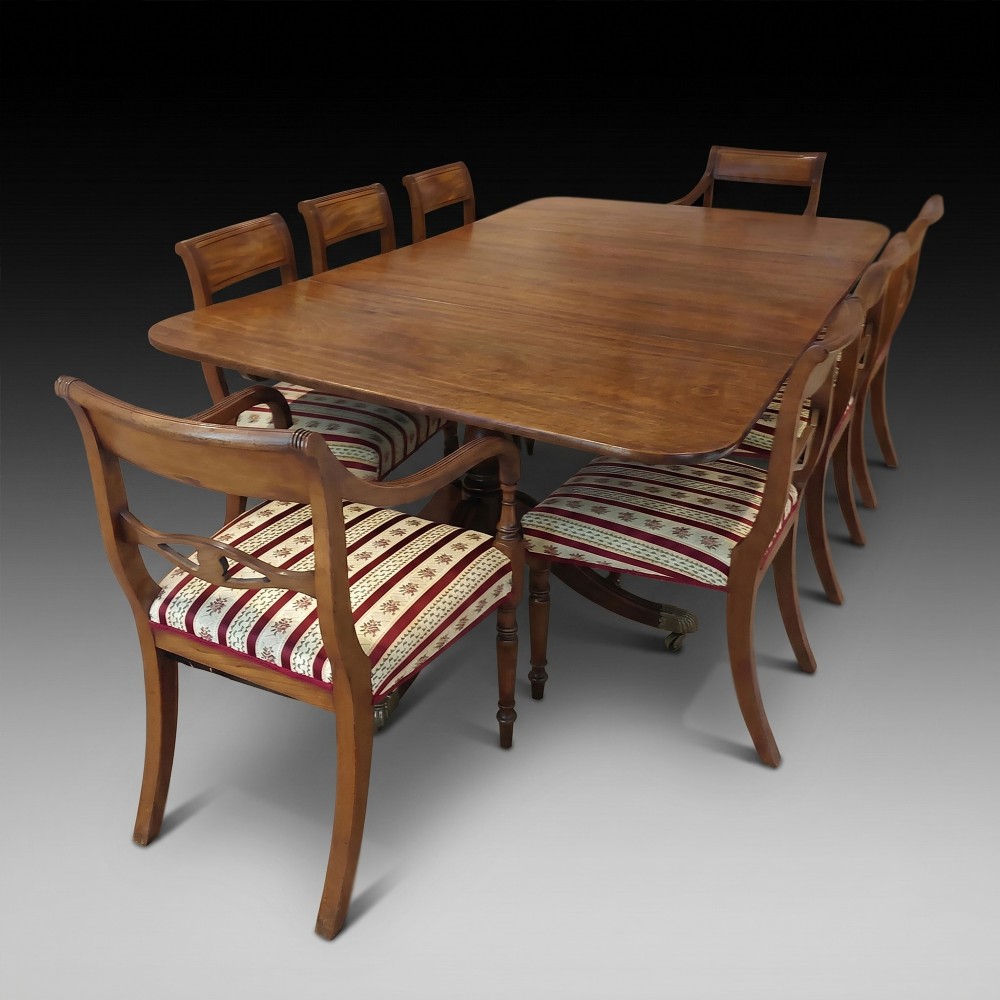 A Regency mahogany extendable dining table surrounded by matching dining chairs with striped upholstered seats.