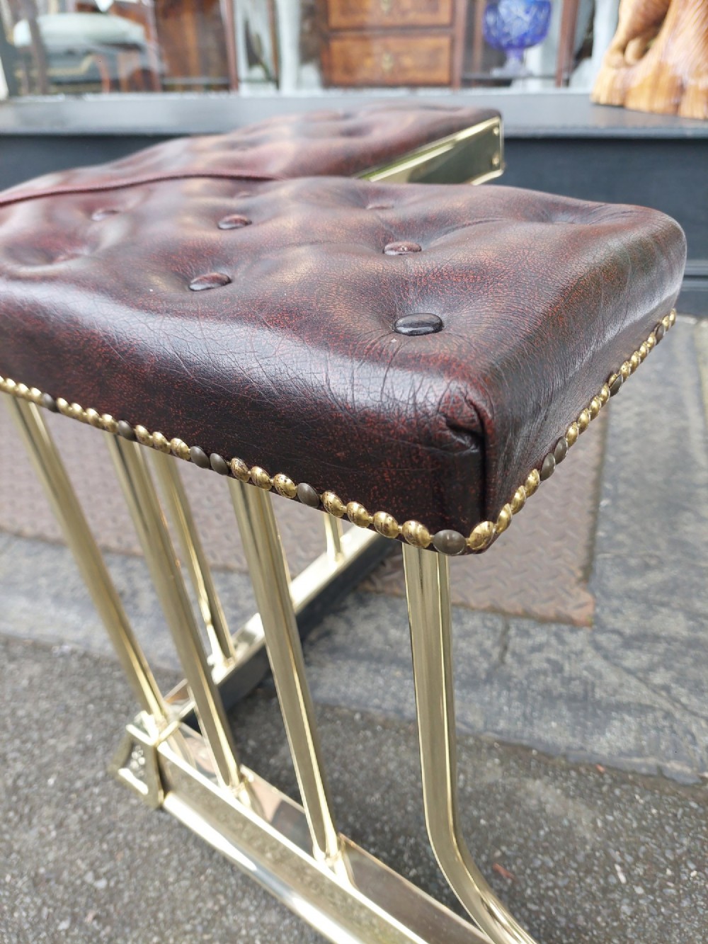 An early 20th-century brass club fender featuring a central dipped rail, vertical brass balusters, and two button-tufted dark red leather upholstered corner seats. View VI