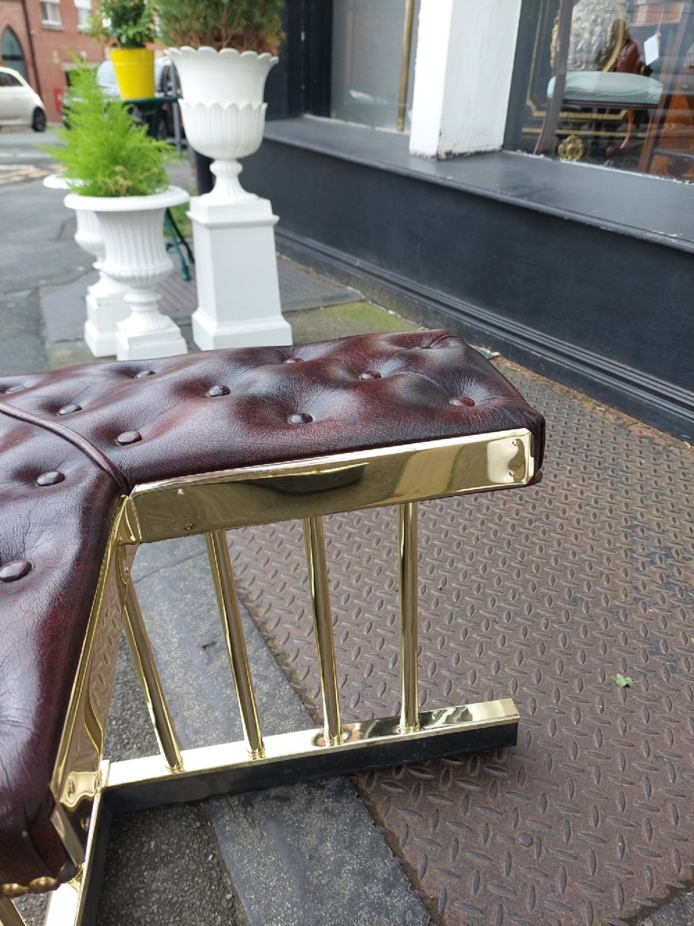 An early 20th-century brass club fender featuring a central dipped rail, vertical brass balusters, and two button-tufted dark red leather upholstered corner seats. View VII