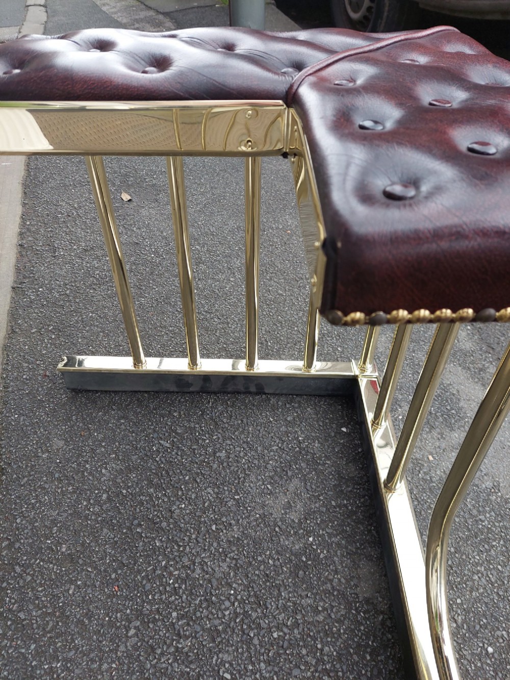An early 20th-century brass club fender featuring a central dipped rail, vertical brass balusters, and two button-tufted dark red leather upholstered corner seats. View IX
