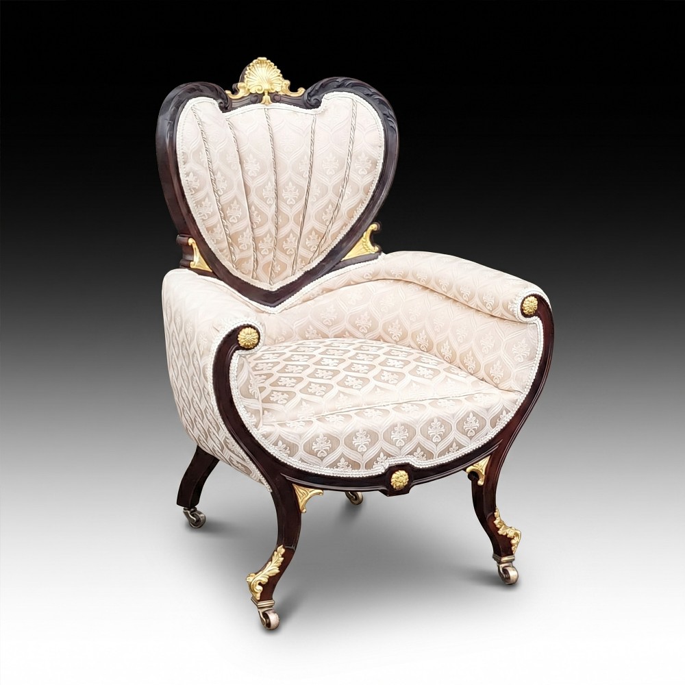 An upholstered French Empire style mahogany armchair featuring gilt bronze mounts, a channelled backrest, cream fabric, and brass castors.