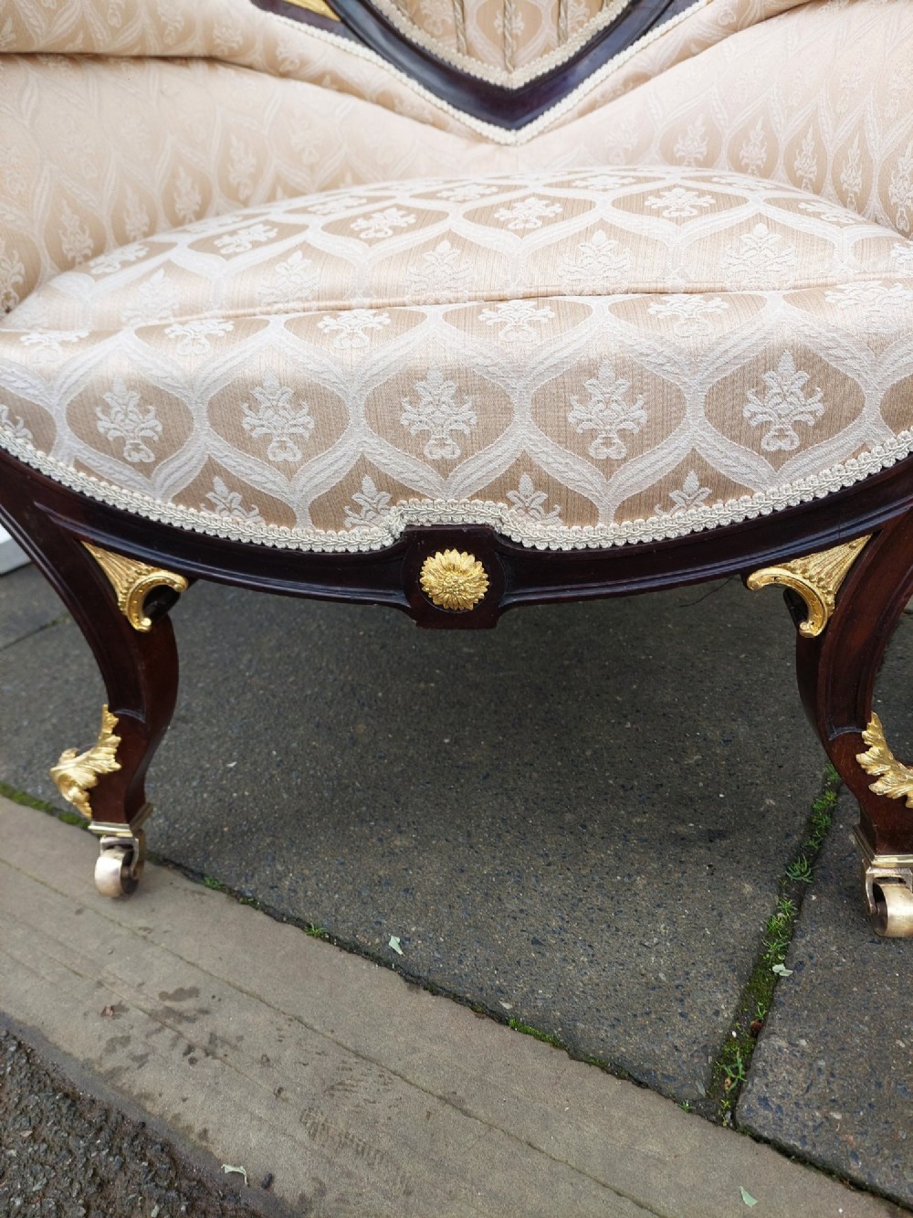 An upholstered French Empire style mahogany armchair featuring gilt bronze mounts, a channelled backrest, cream fabric, and brass castors. View V