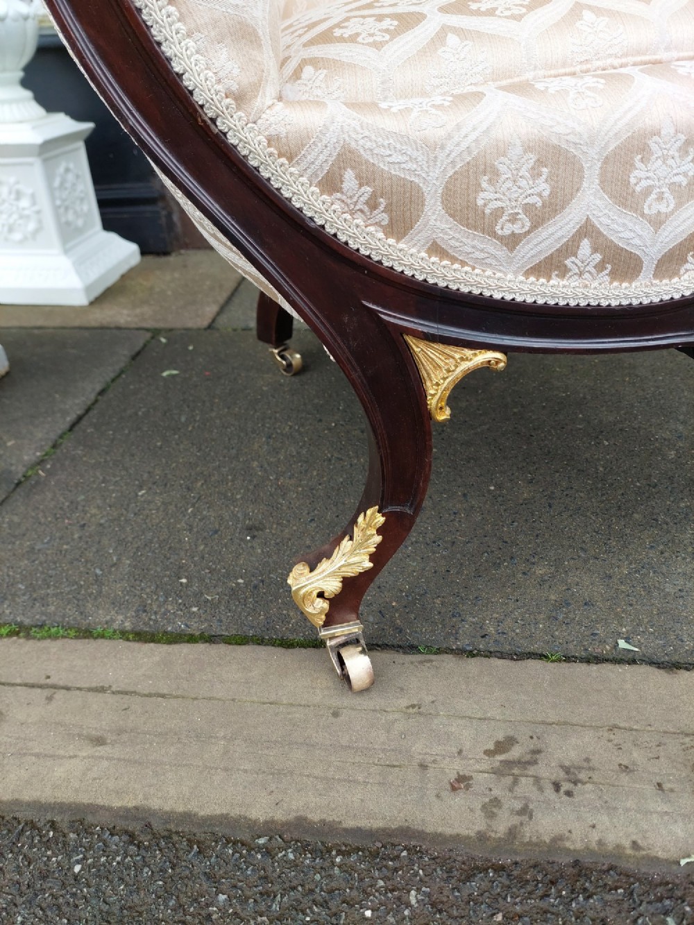 An upholstered French Empire style mahogany armchair featuring gilt bronze mounts, a channelled backrest, cream fabric, and brass castors. View VI