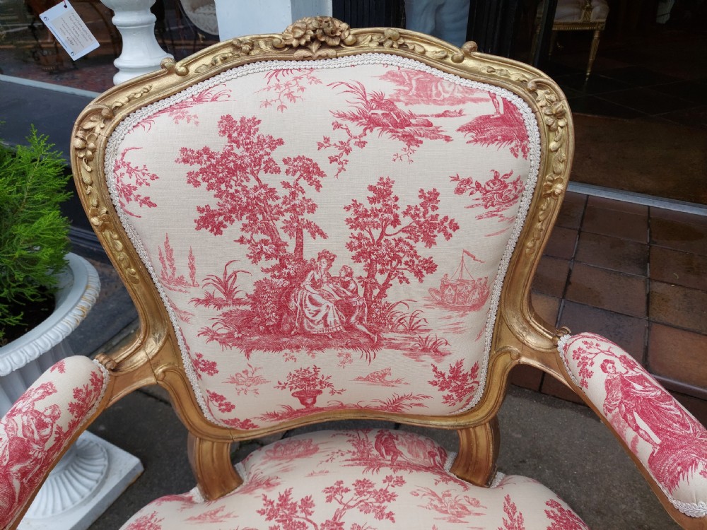 A late 19th-century French Rococo Revival giltwood open armchair upholstered in red and white Toile de Jouy patterned fabric featuring cabriole legs and floral carvings. View V