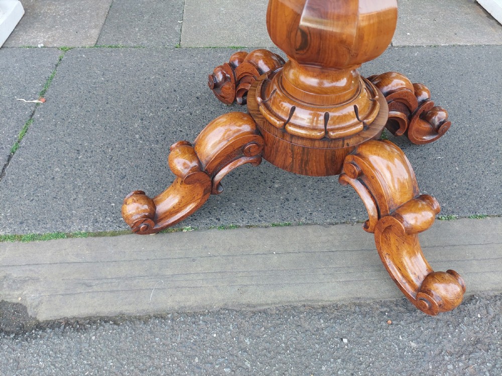 A 19th-century William IV rosewood tea table featuring a polished rectangular fold-over top, carved scrollwork frieze, bulbous faceted pedestal stem, and scroll feet on brass castors. View IV