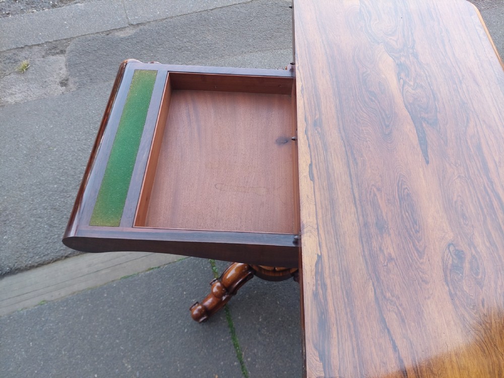 A 19th-century William IV rosewood tea table featuring a polished rectangular fold-over top, carved scrollwork frieze, bulbous faceted pedestal stem, and scroll feet on brass castors. View VIII