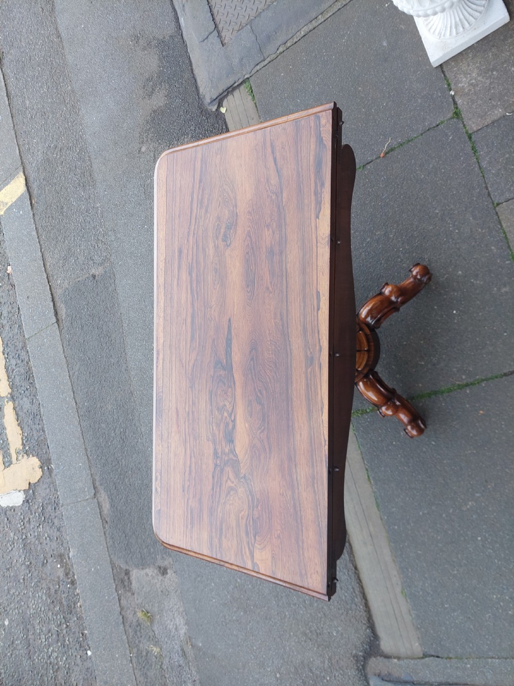 A 19th-century William IV rosewood tea table featuring a polished rectangular fold-over top, carved scrollwork frieze, bulbous faceted pedestal stem, and scroll feet on brass castors. View IX