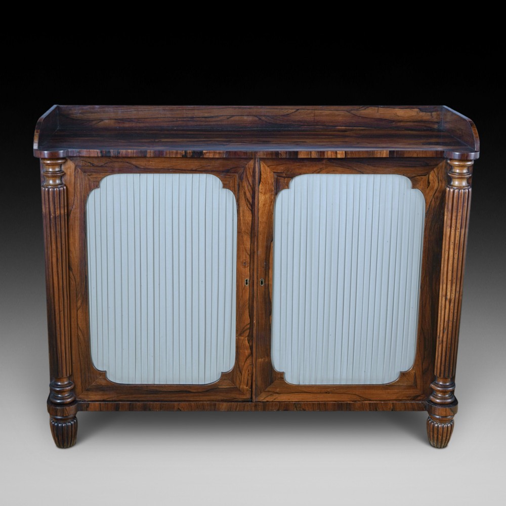 A Regency Goncalo Alves side cabinet featuring two pleated light fabric panel doors flanked by fluted columns on turned feet.