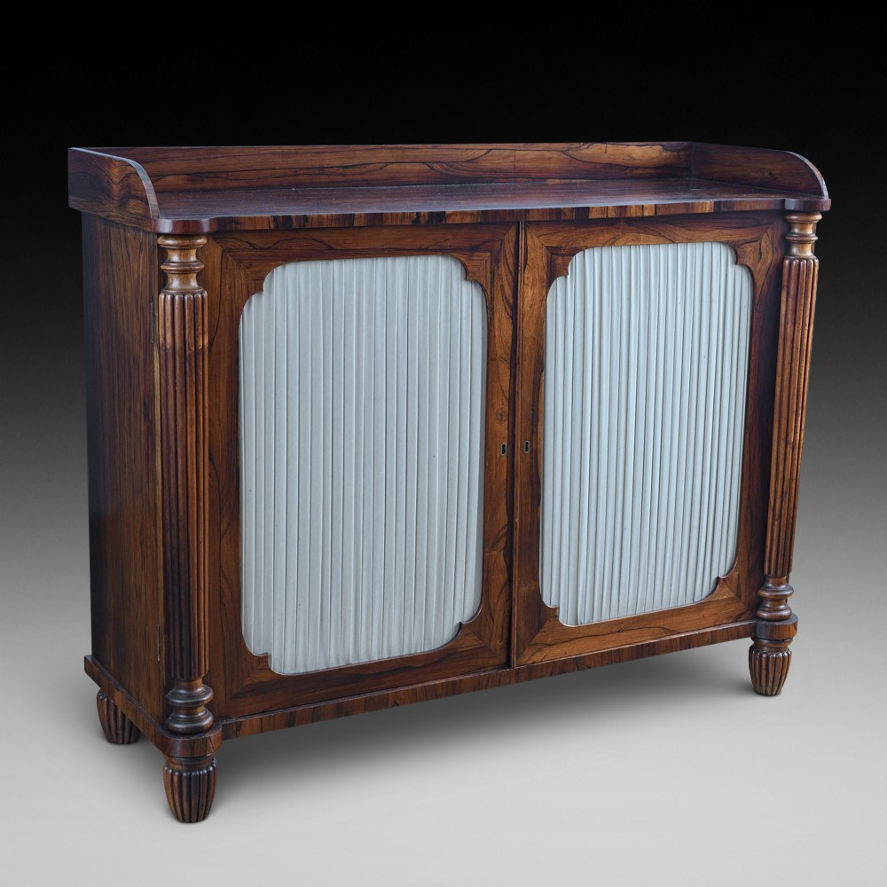 A Regency Goncalo Alves side cabinet featuring two pleated light fabric panel doors flanked by fluted columns on turned feet. View II