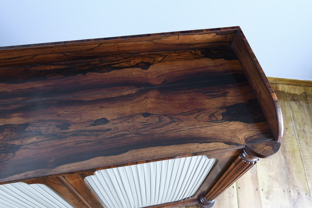 A Regency Goncalo Alves side cabinet featuring two pleated light fabric panel doors flanked by fluted columns on turned feet. View III