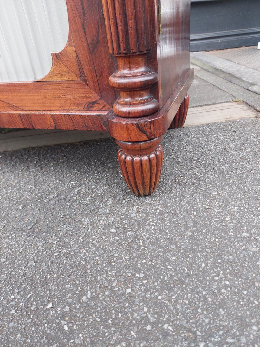 A Regency Goncalo Alves side cabinet featuring two pleated light fabric panel doors flanked by fluted columns on turned feet. View V