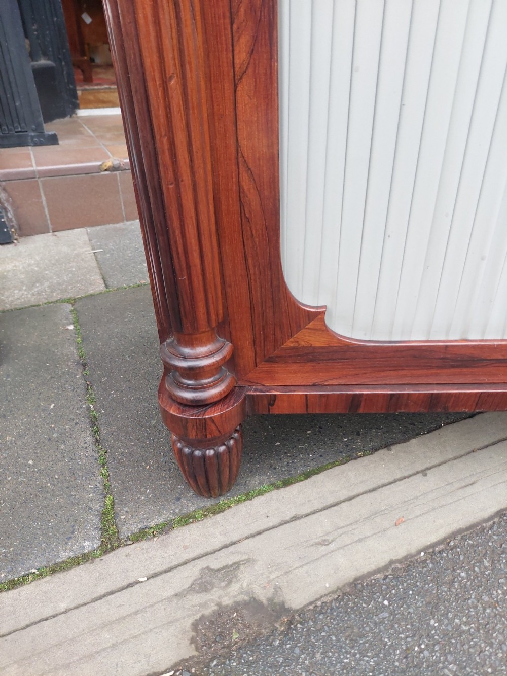 A Regency Goncalo Alves side cabinet featuring two pleated light fabric panel doors flanked by fluted columns on turned feet. View VI