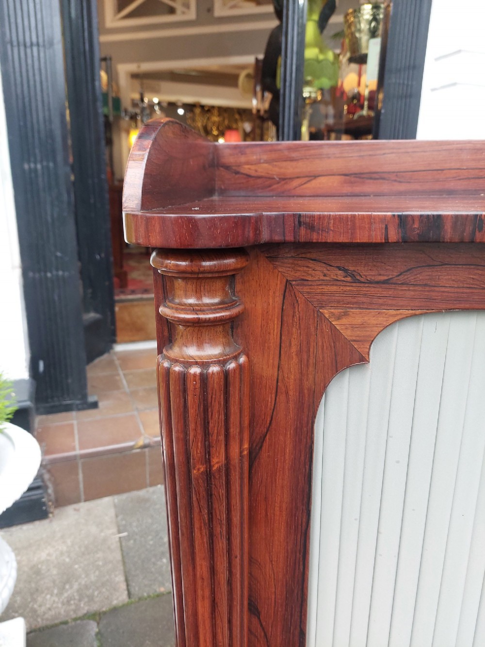 A Regency Goncalo Alves side cabinet featuring two pleated light fabric panel doors flanked by fluted columns on turned feet. View VII