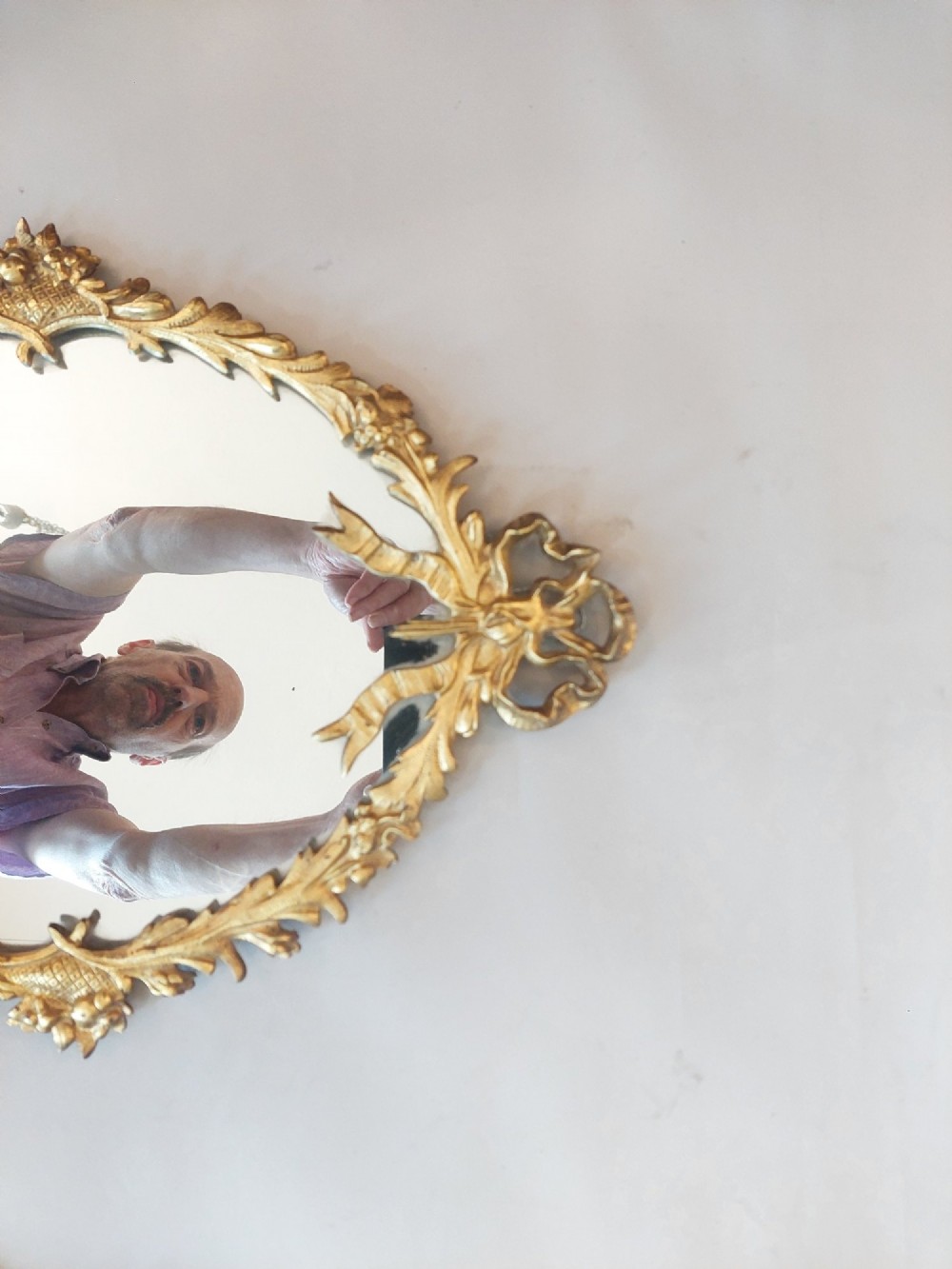 A pair of early 20th-century oval gilt metal wall mirrors with ribbon-tied crests and three candle branches. View II