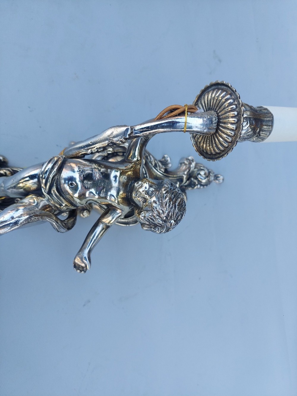 A pair of early 20th-century silvered metal wall sconces featuring sculpted cherubs holding single candle sockets set against elaborate scrollwork backplates. View II